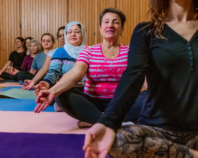 Mehrere ältere Menschen üben gemeinsam Tai Chi in einem hellen Raum mit Holzboden und großen Fenstern.