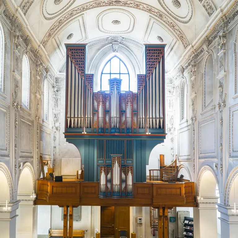 Blick in das helle Kirchenschiff mit hölzernen Bänken und großer Orgel auf einer Empore.
