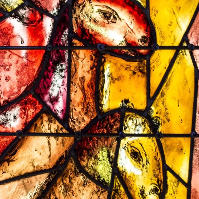 Buntes Glasfenster mit stilisierten Pferdeköpfen, vorwiegend in Rot-, Gelb- und Brauntönen gehalten.