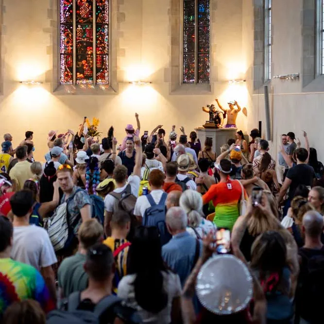 Eine grosse Menschenmenge feiert in einer Kirche mit bunten Kleidern und erhobenen Armen.