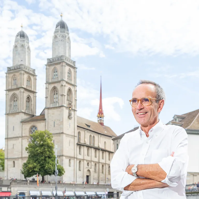 Christoph Schneider, Leiter vom Freundeskreis, steht vor dem Zürcher Grossmünster mit blauem Himmel und historischen Gebäuden im Hintergrund.